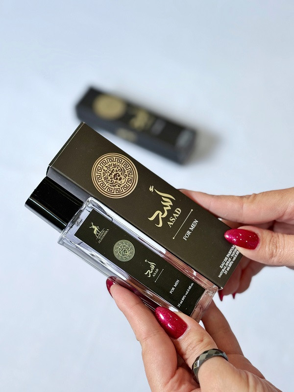 تصویر ادکلن مردانه الحمبرا مدل اسد در دست یک خانم با پس زمینه سفید