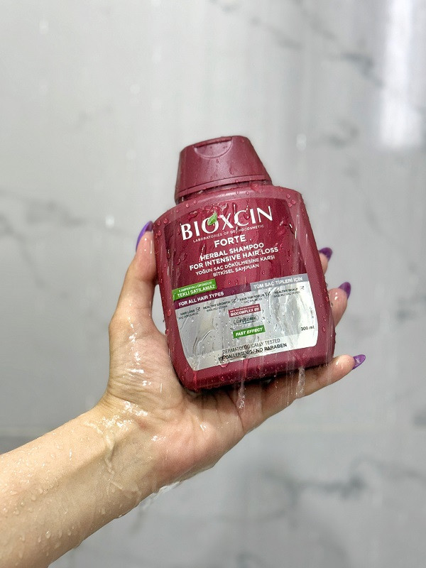تصویر واقعی شامپو ضد ریزش بیوکسین در دست مصرف کننده زیر دوش حمام؛ نشان دهنده کاربرد روزانه برای تقویت مو